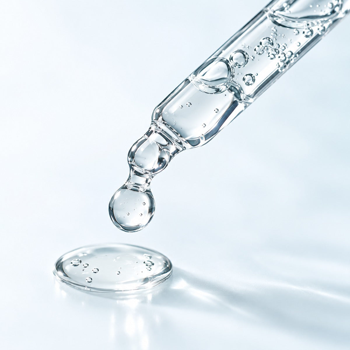 Glass pipette and clear serum on a light background, an illustrative skincare texture